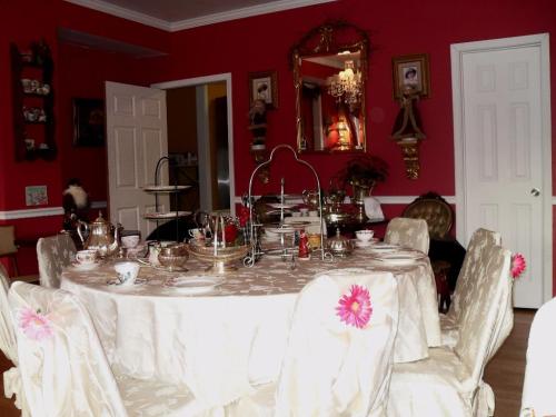 A dining room with a round table set for tea, adorned with a floral tablecloth and pink decorations on the chairs.