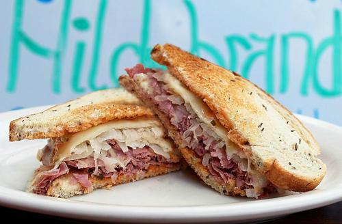 A close-up of a sliced sandwich with layers of corned beef, sauerkraut, and Swiss cheese on toasted rye bread.