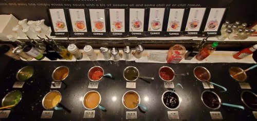 A variety of colorful sauces and condiments in bowls on a counter, with bottles and labels in the background.