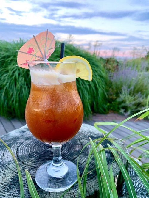 A refreshing cocktail with an umbrella and lemon slice, set against a scenic outdoor background at sunset.