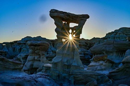 A stunning rock formation with a sunburst shining through, set against a blue sky and unique geological features.