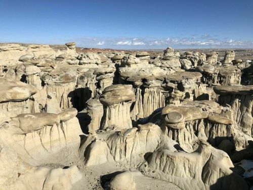 A vast landscape of unique rock formations with hoodoos under a clear blue sky.