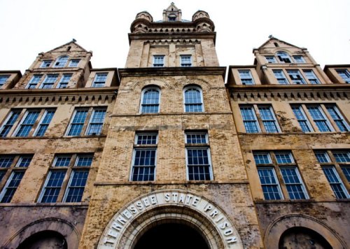 Historic Tennessee State Prison building with tall towers and large windows, viewed from below against a gray sky.