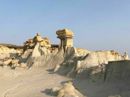 Unique rock formations rise from a sandy landscape under a clear blue sky, showcasing natural erosion patterns.