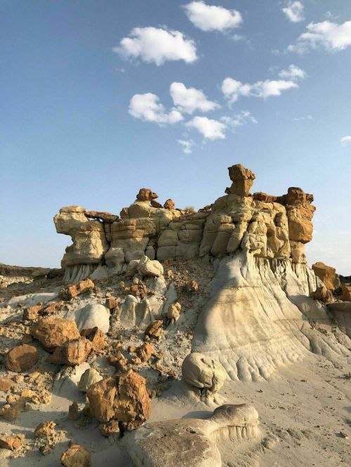 Rocky formations with layered textures and colors under a blue sky with scattered clouds.