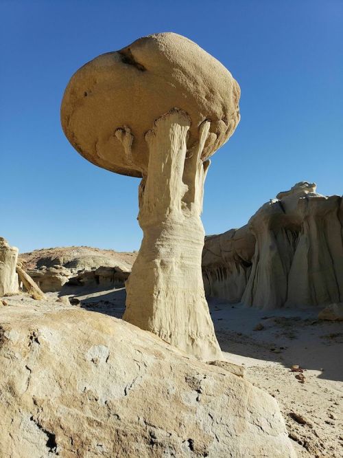 A unique rock formation resembling a mushroom, with a wide cap and a slender base, set against a clear blue sky.