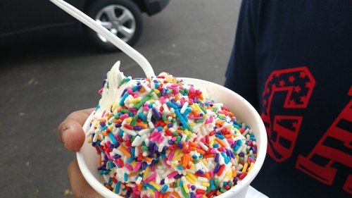 A hand holding a cup of ice cream topped with colorful sprinkles and a plastic spoon.
