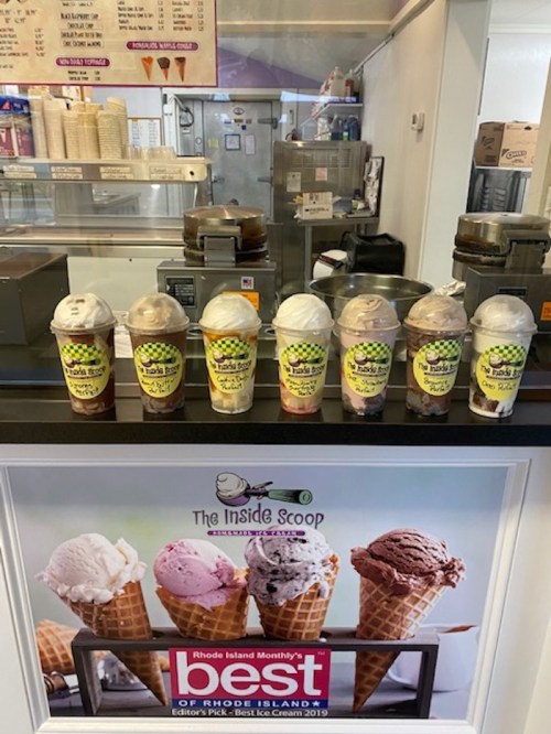 A display of eight ice cream cups in front of a shop counter, with a sign highlighting an award for best ice cream.