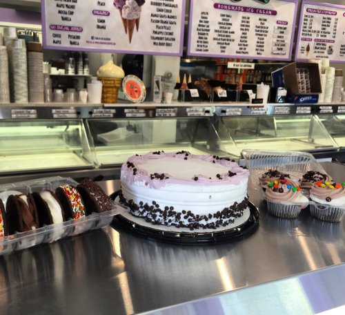 A display of ice cream cakes and treats, including a round cake and assorted ice cream sandwiches, in a shop.