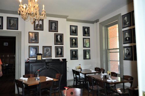 A cozy restaurant interior featuring wooden tables, chairs, and a wall adorned with framed portraits.