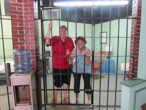 Two people playfully posing behind jail bars in a staged prison setting, smiling and holding onto the bars.