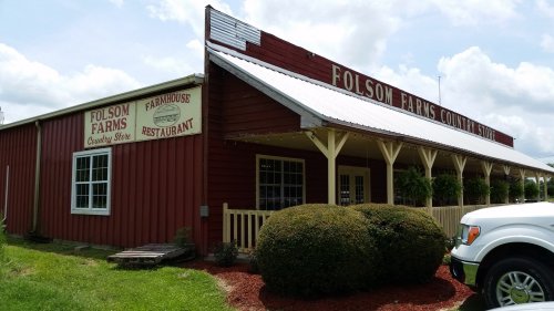 Red barn-style building with "Folsom Farms Country Store" and "Farmhouse Restaurant" signs, surrounded by greenery.