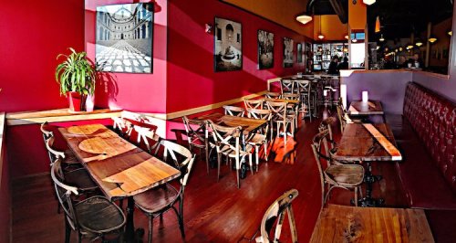 Cozy restaurant interior with wooden tables, red walls, and artwork, featuring a bright and inviting atmosphere.