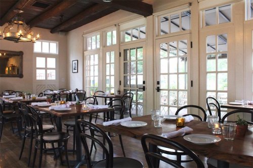 Cozy restaurant interior with wooden tables, chairs, and large windows, creating a warm and inviting atmosphere.