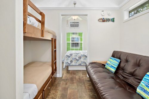 Cozy interior of a small room featuring bunk beds, a sofa, and a bed with colorful pillows and bright decor.