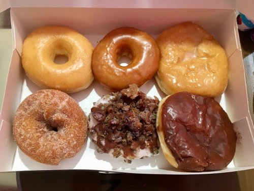 A box of assorted donuts: two glazed, one chocolate frosted, one cinnamon sugar, and one with chocolate and toppings.