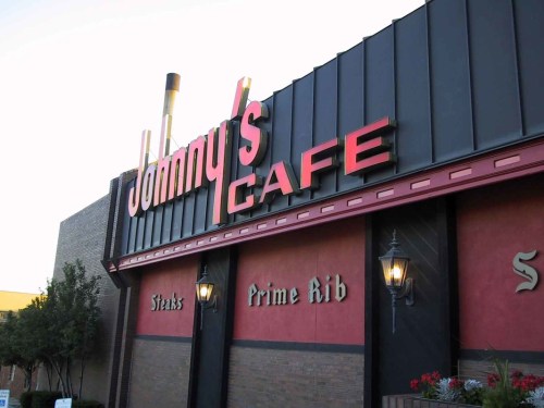 Signage of Johnny's Cafe featuring "Steaks" and "Prime Rib" with a brick exterior and decorative lanterns.