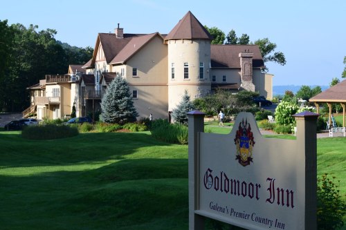 A scenic view of Goldmoor Inn, a charming country inn with lush green lawns and trees in the background.