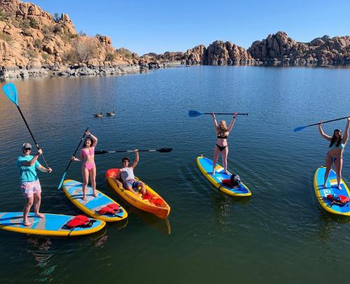 Five people paddleboarding on a calm lake surrounded by rocky formations, enjoying a sunny day.