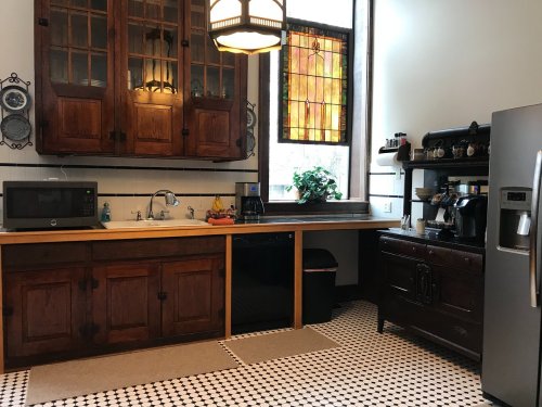 A cozy kitchen featuring wooden cabinets, a sink, a microwave, and a coffee station, with stained glass windows.