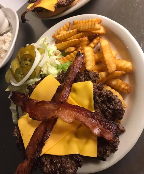 A plate of a cheeseburger topped with bacon, lettuce, jalapeños, and crinkle-cut fries on the side.