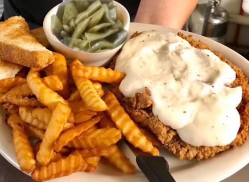 A plate of crispy fried chicken topped with creamy gravy, served with crinkle-cut fries, green beans, and toast.