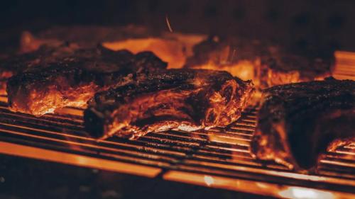 Grilled steaks sizzling on a barbecue, with flames and smoke creating a warm, inviting atmosphere.