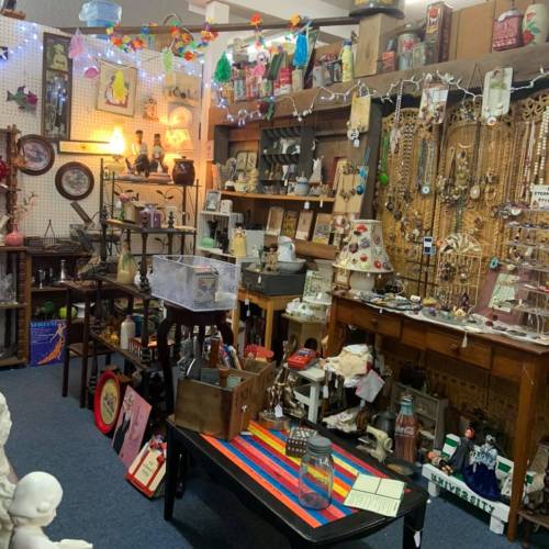 A cozy vintage shop filled with eclectic decor, jewelry, and various antiques displayed on shelves and tables.