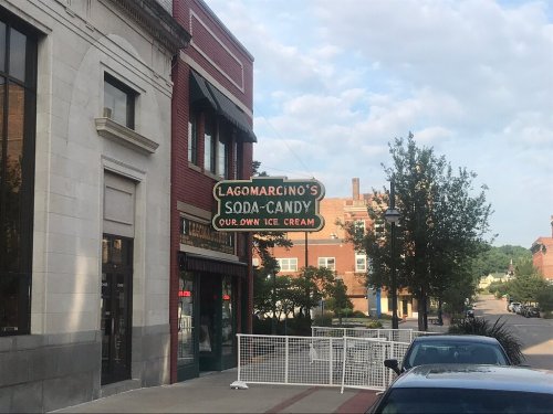 Sign for Lagomarcino's Soda-Candy, featuring "Our Own Ice Cream," on a street with trees and buildings in the background.