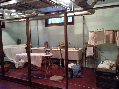 A vintage laundry room with two sinks, a washboard, and hanging clothes, featuring wooden beams and industrial pipes.