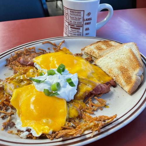 A plate of cheesy hash browns topped with two eggs, sour cream, and green onions, alongside a slice of toast and a coffee mug.