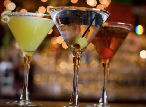 Three elegant cocktails in stemmed glasses, featuring a green drink, a classic martini with an olive, and a reddish drink.
