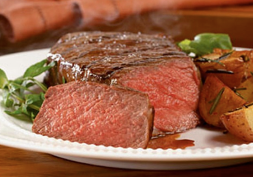 A perfectly cooked steak with a side of roasted potatoes, garnished with herbs, on a white plate.