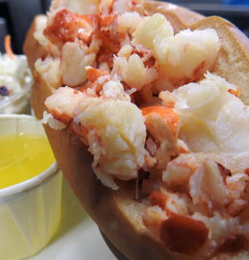 Close-up of a lobster roll filled with chunks of lobster meat, served with a side of yellow dipping sauce.