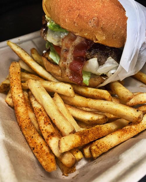 A juicy burger with lettuce, tomato, and bacon, served with a side of seasoned French fries.