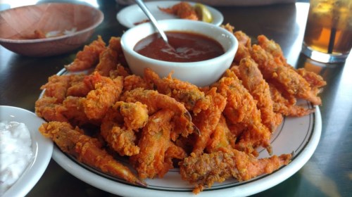 A plate of crispy orange fried shrimp with a small bowl of dipping sauce in the center.
