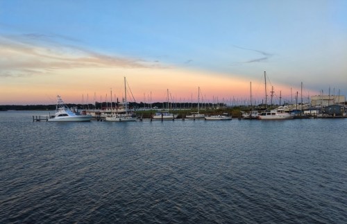 A serene marina at sunset, featuring various boats and masts against a colorful sky.