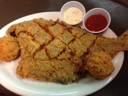 A large, fried fish served on a plate with two dipping sauces: tartar and ketchup.