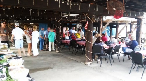 A lively gathering under a covered patio with people socializing, dining, and enjoying a festive atmosphere.