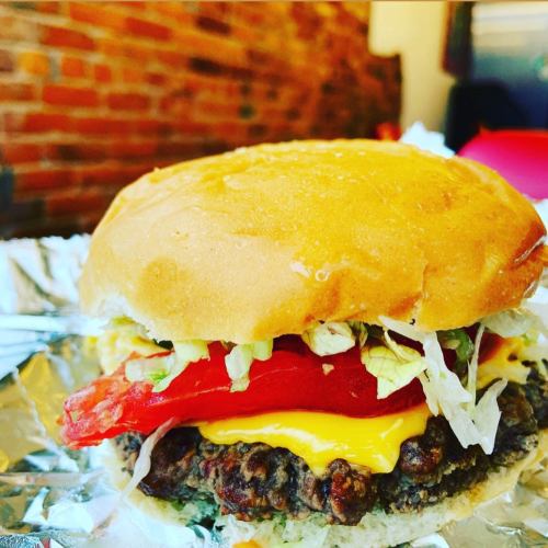 A close-up of a cheeseburger with lettuce, tomato, and melted cheese on a toasted bun, resting on foil.