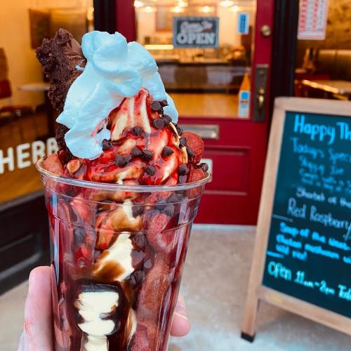 A delicious ice cream sundae topped with whipped cream, chocolate chips, and a brownie, held in front of a shop entrance.