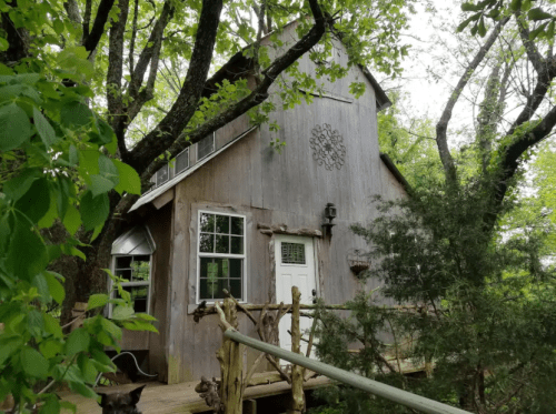 A rustic wooden cabin nestled among trees, featuring large windows and a porch with a railing.
