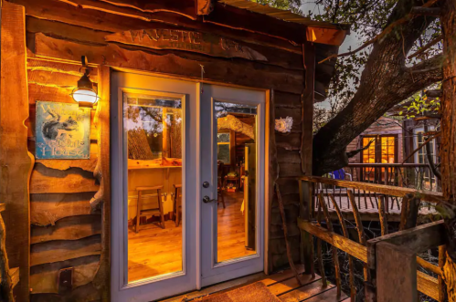Cozy wooden cabin entrance with warm lighting, surrounded by trees and a rustic deck.