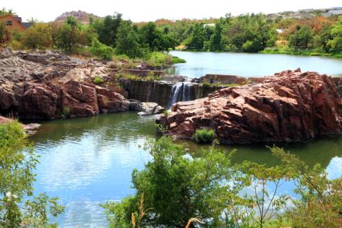 A serene landscape featuring a small waterfall cascading into a calm lake, surrounded by rocky formations and lush greenery.