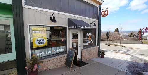Exterior of a pretzel shop with a sign for National Pretzel Day, featuring a black awning and a chalkboard menu.