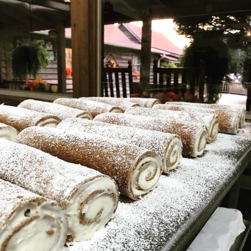A tray of freshly baked cinnamon rolls dusted with powdered sugar, set in a cozy outdoor setting.