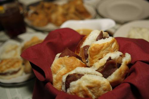 A basket of flaky biscuits filled with meat, surrounded by plates of food on a dining table.
