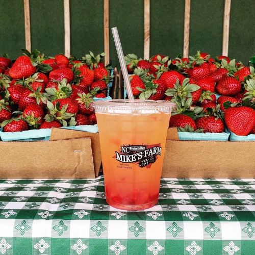 A refreshing drink in a clear cup sits on a checkered tablecloth, with fresh strawberries in the background.
