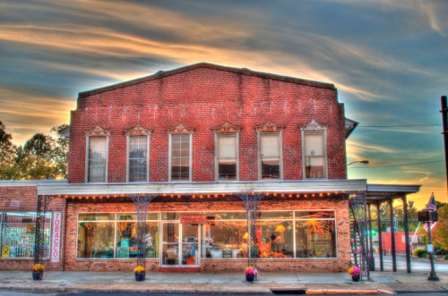 Historic brick building with large windows, displaying flowers and decor, under a colorful sunset sky.