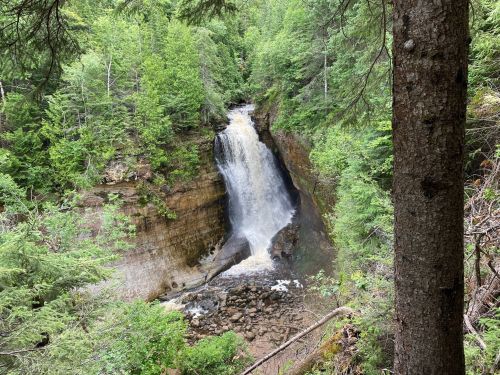 A scenic waterfall cascading down rocky cliffs, surrounded by lush green trees and foliage.